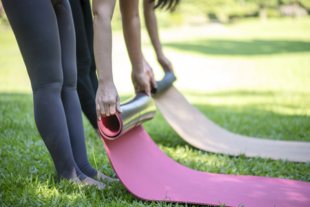 Young yoga woman standing rolling her pink mat after a yoga exercise  outdoors in nature, close upの写真素材