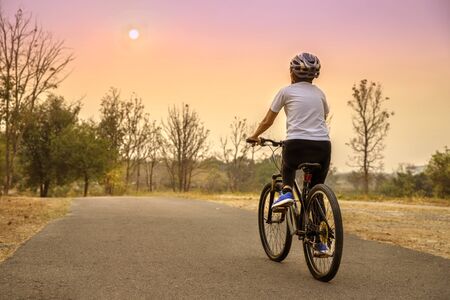Back view of  woman riding on bike in the nature  park at summer sunset. Blurred background with copy space area for a text.の写真素材