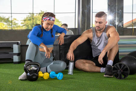 athletic young couple drinking water and resting with weight exercise after workout in gym