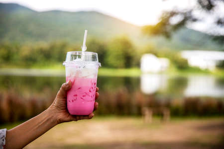 Close up hand of woman holding strawberry smoothie in plastic cup. over nature...