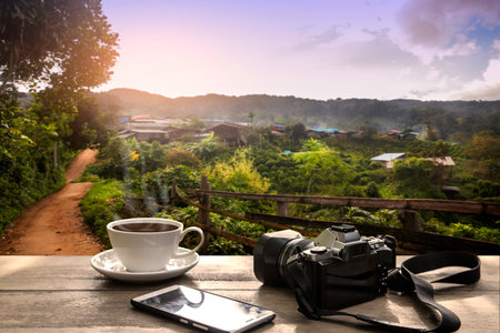 coffee Cup with mobile phone and camera  on wood table over mountains landscape with sunlight...