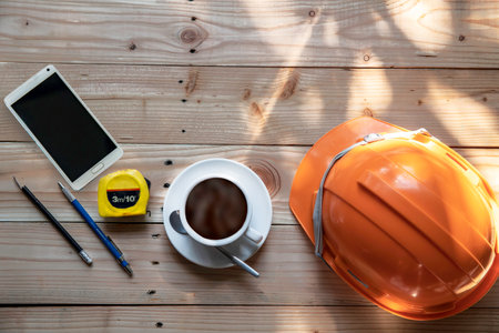 Top view Safety Engineer Helmet,cup of coffee,pencil and Measure the cable. on brown wooden table background. Space for design. - Imageの写真素材