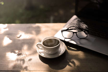 Hot coffee cup with laptop computer and eye glasses on wood table on morning summer. relaxation...