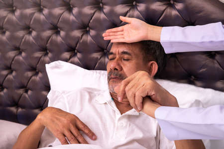 Elderly man in bed examined by doctor with her hand.  health care conceptの写真素材