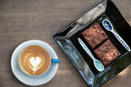 latte art coffee cup with brownie in dish on wooden table at coffee shop. relaxation concept