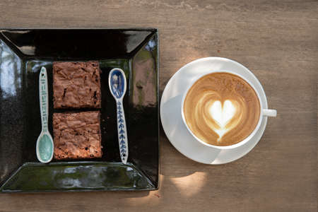 latte art coffee cup with brownie in dish on wooden table at coffee shop.. relaxation conceptの写真素材