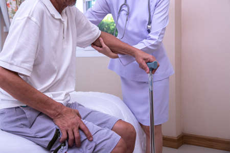 Young  nurse assisting senior man to get up from bed. Caring nurse supporting patient while getting up from bed . Helping elderly disabled man standing up.の写真素材
