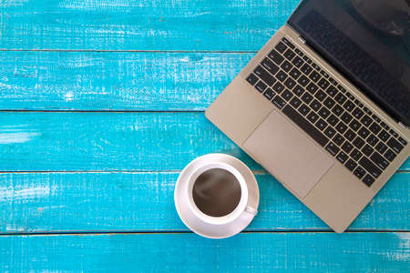 Top view  of hot coffee cup and laptop on blue table with copy space, flat lay.