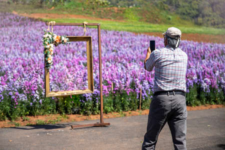 A man taking a picture of the flowers in park with his smartphone.,. holiday conceptの写真素材
