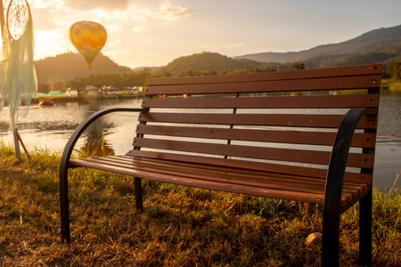 a chair beside lake with yellow sunlight through the branch on a nice sunny day at the nature park . imageの写真素材
