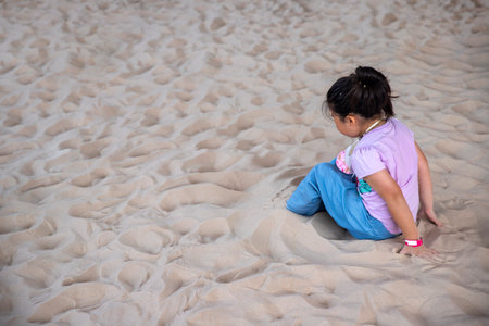 A little  girl sitting on the beach on sand in summer holidaysの写真素材