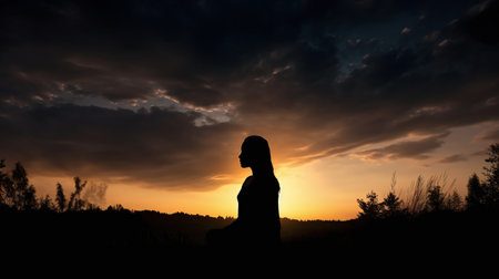 Silhouette of a woman praying at sunset in the mountains.の素材