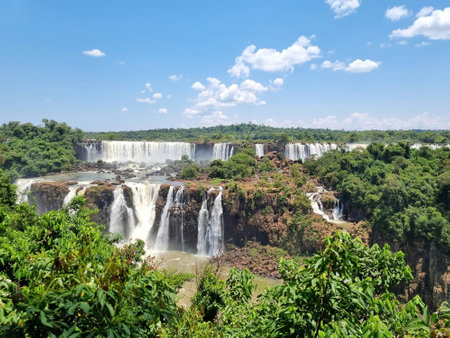 Through the green vegetation, a view of the Argentina side of the Iguazu Falls, a blue sky with some clouds, from the national park in Brazilの写真素材