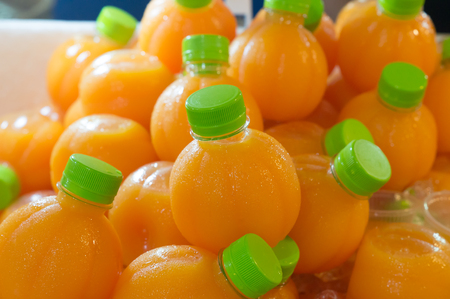 Orange juice in round plastic bottles on sale, sweet orange juice in round plastic bottles soaked into ice for refreshmentの写真素材