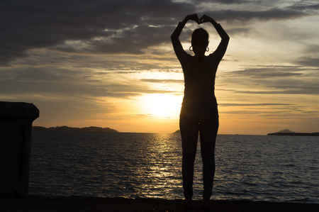A woman standing with her hands like heart shape over her head at twilight at the seaの写真素材