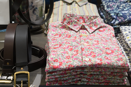 Stacking shirts with colorful pattern and leather belt in orderly piles are on sale in department store, Colorful shirts are stacking in order on sale in a shopの写真素材