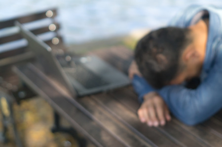 A man is taking a break by sitting with falling his head down on the desk after using laptop in a public park, blurred pictureの写真素材