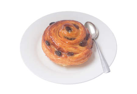 Spiral danish pastry or sweet bun with raisin on top on white plate with small teaspoon served for breakfast is isolated on white background.の写真素材