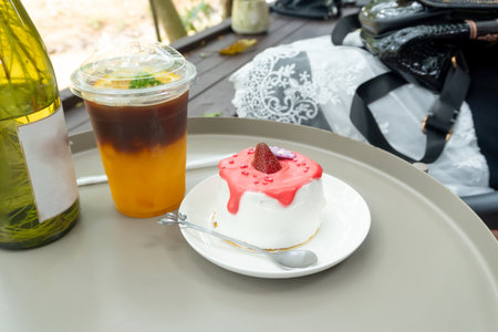 Iced lemon tea in transparent plastic glass and strawberry cake with glazed cream in mini white...