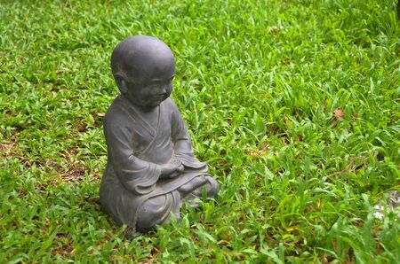 Black stone little buddha on green grassの写真素材
