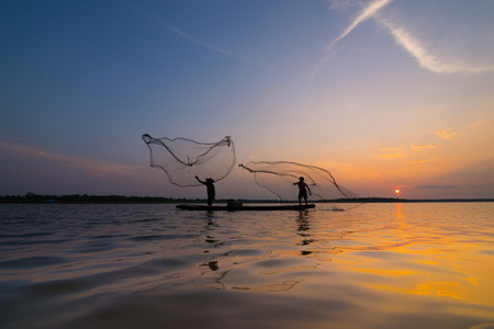 Silhouette of a fisherman throwing his net with sunset.の写真素材