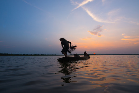 Silhouette of a fisherman throwing his net with sunset.の写真素材