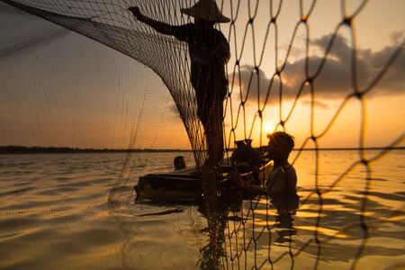 Silhouette of a fisherman throwing his net with sunset.の写真素材