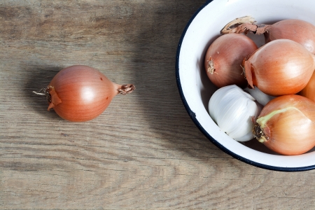 old fashioned still life with onion and garlic in enamel bowl on rustic woodの写真素材