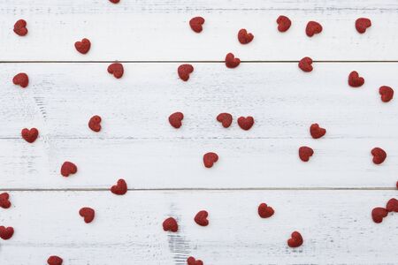 Red little hearts on white wooden background from top view
