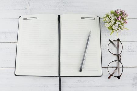 Open notebook, glasses, pens and white sweet williams flowers bouquet on white wood backgroundの写真素材