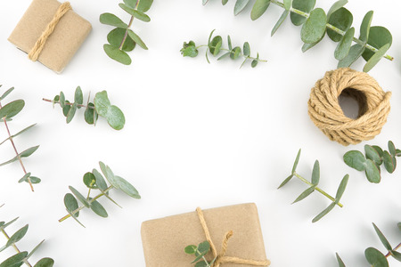 Brown gift boxes and ropes decorated with baby eucalyptus leaves with copy space in the center on white backgroundの写真素材