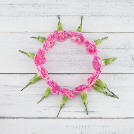 Round wreath made from pink carnation flowers on white wood background with copy spaceの写真素材
