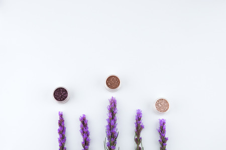 Eye shadow glitter set decorated with violet liatris flowers on white background with copy space