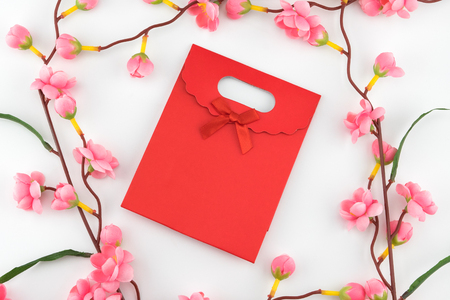 Red gift bag decorated with fake pink flower branches on white backgroundの写真素材