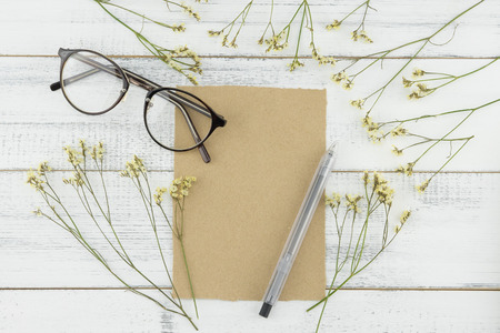 Blank brown card, pen and eyeglasses decorated with yellow limonium caspia flowers on white wood backgroundの写真素材