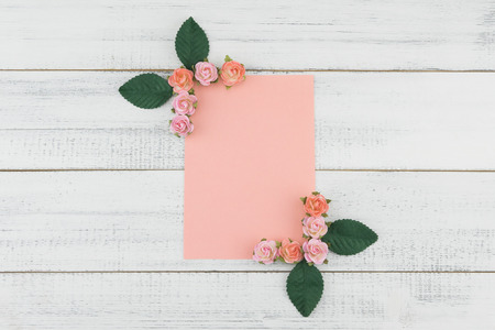 Blank pink card decorate with pink rose paper flowers and green leaves on white wood background