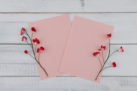 Two blank pink card decorate with red paper flowers on white wood background