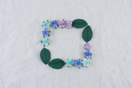 Square wreath made from blue tone rose paper flowers and green leaves on muslin fabric with copy...