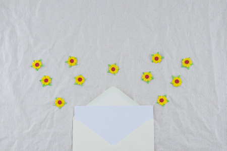 White card in yellow envelop decorate with yellow paper flowers on muslin fabric with copy space