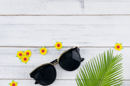 Sunglasses decorate with fern leaves and yellow paper flowers on white wood background with copy spaceの写真素材