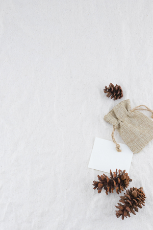 Blank white card, sackcloth bag and pinecones on muslin fabric background with copy spaceの写真素材