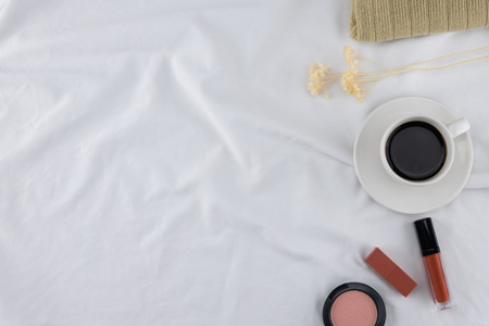 A cup of coffee with cosmetics on white bed with copy spaceの写真素材
