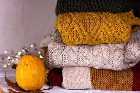 Autumn. Pumpkins, dray leaves and knitted sweaters decorated Christmas fairy string lights on white wooden background.の写真素材