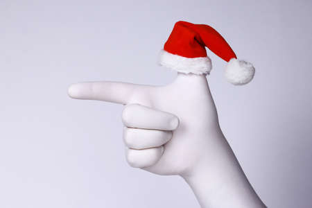 Pointing hand with Santa Claus heat on finger. Hand in white glove and Santa Claus heat pointing on white background. Christmas and New Year holidays concept.の写真素材