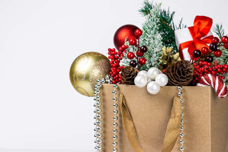 Christmas and New Year decoration. Craft paper shopping bag with gifts, toys, green spruce branches, red berries and golden fir cones. Winter holidays shopping and gifts concept.の写真素材