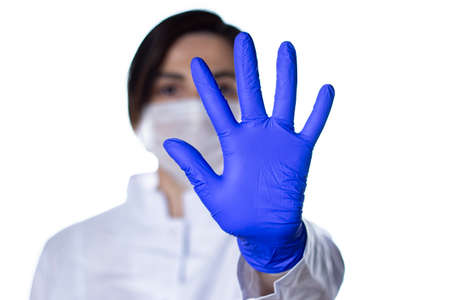 Young woman doctor or nurse in protective white medical face mask showing stop sign. with her hand with coronavirus.の写真素材