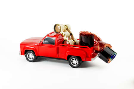 Retro opera glasses and film in red trendy pickup trunk. Toy truck, film roll and retro binoculars. Part of set.の写真素材