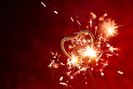 Heart shape Bengal light sparkle on red abstract background. Holiday greeting card, background for Valentine's and Wedding day. Romantic metaphor concept. Part of set.の写真素材