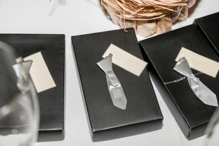 Small gray paper ties, on black gift boxes and white labels with copy space at a celebration.