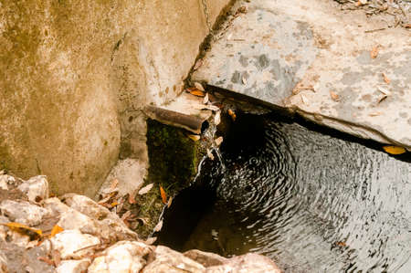 Clean, clear water flowing from a traditional stone-lined metal spout or pipe in the forest in...